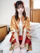 A woman in a red and gold dress sitting on a bed.